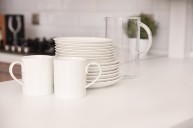 Stack of clean dishes, cups and glass jug on table in kitchen