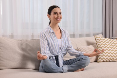 Photo of Woman meditating on sofa at home. Harmony and zen
