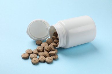 Photo of Bottle and vitamin pills on light blue background