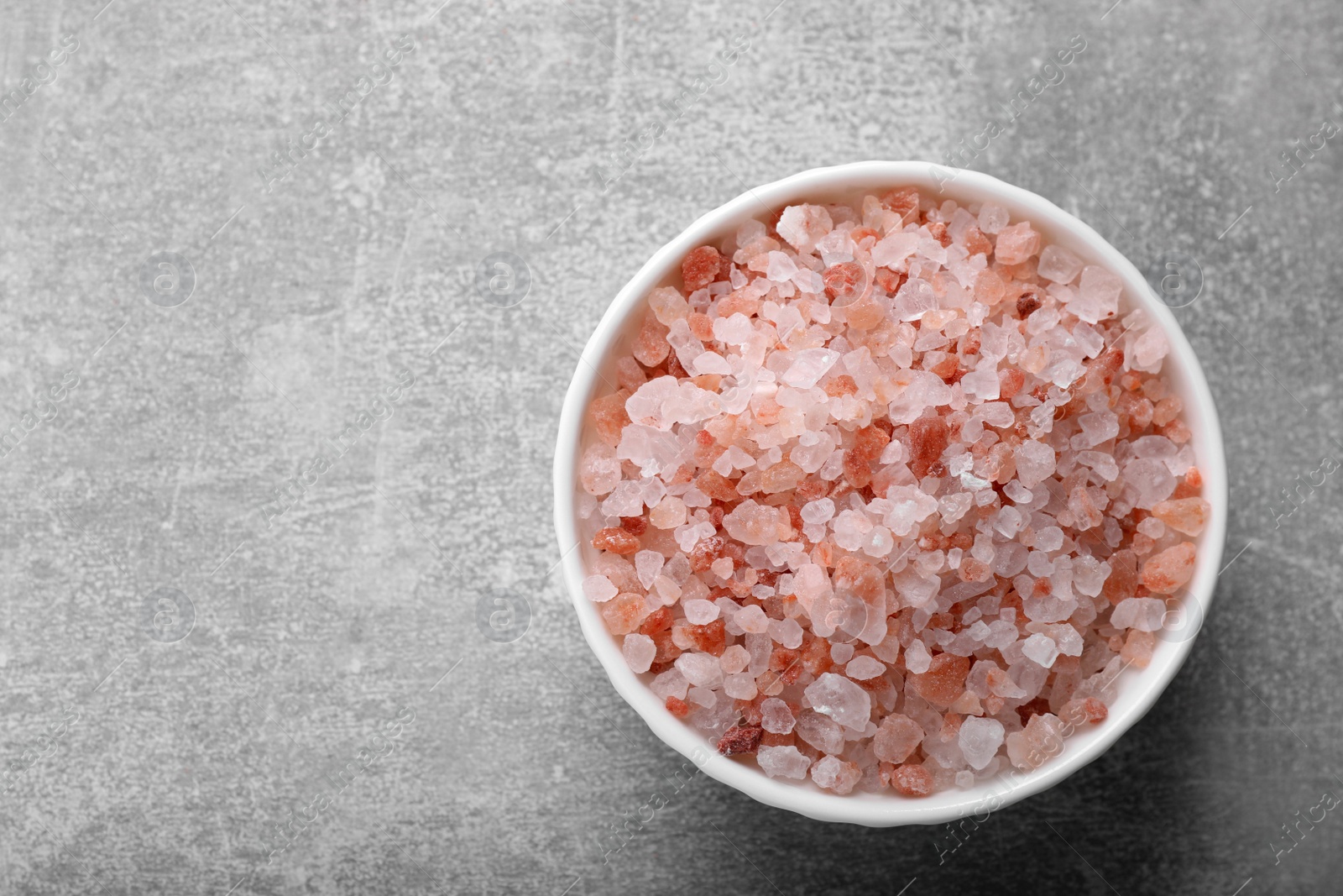 Photo of Pink Himalayan salt in bowl on grey table, top view. Space for text