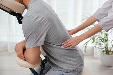 Photo of Man receiving massage in modern chair indoors, closeup