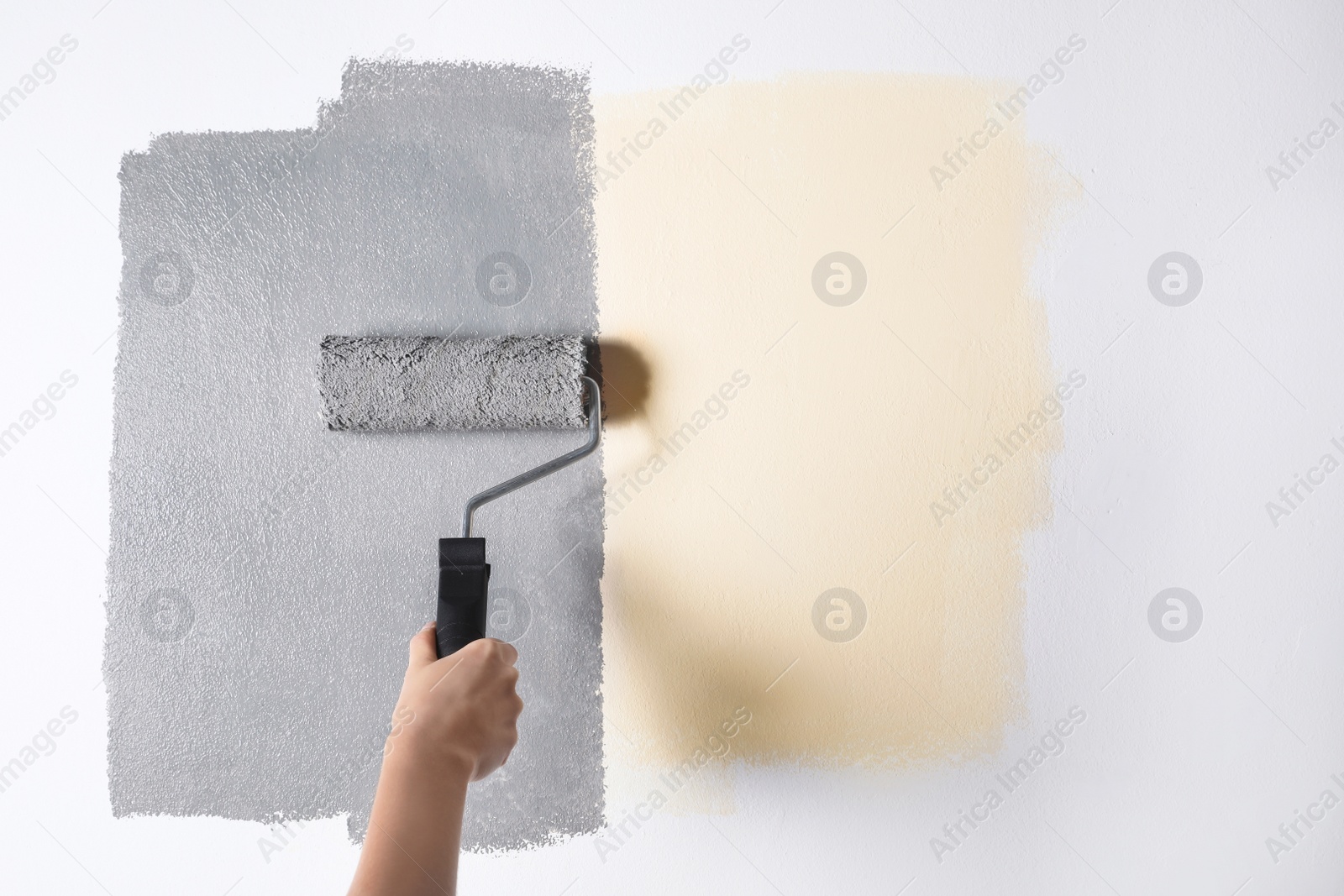 Photo of Woman painting white wall with grey dye, closeup