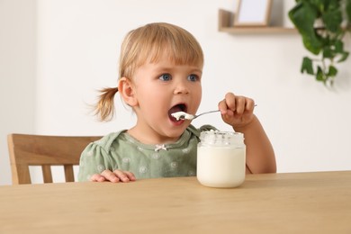 Photo of Cute little child eating tasty yogurt with spoon at wooden table indoors