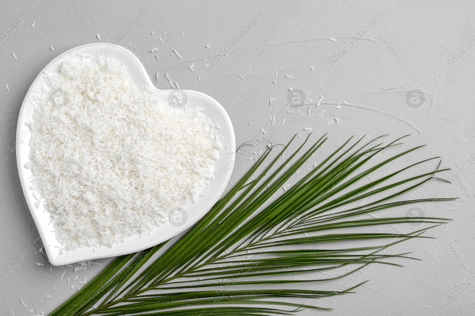 Photo of Heart-shaped plate with fresh coconut flakes on grey background