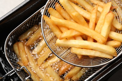 Photo of Delicious freshly prepared french fries in metal strainer, closeup