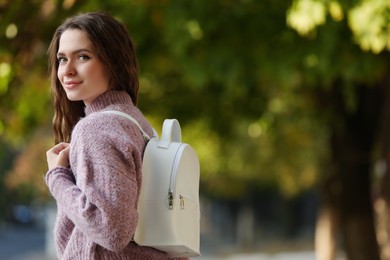 Young woman with stylish white backpack in park, space for text