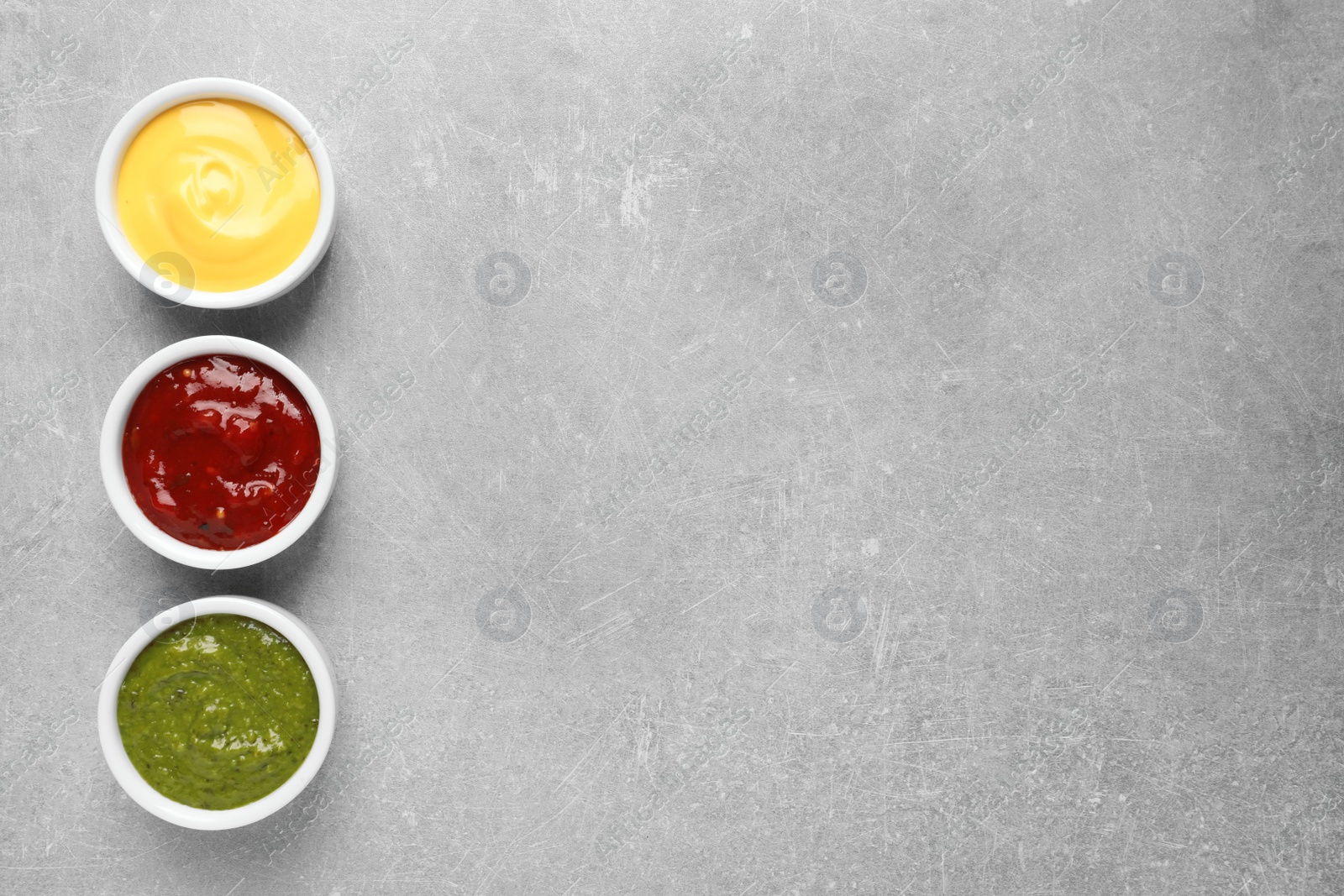 Photo of Set of different delicious sauces on grey table, top view. Space for text