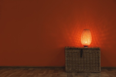 Photo of Modern lamp on wicker chest against color wall indoors. Space for text