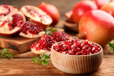 Photo of Delicious ripe pomegranate kernels in bowl on wooden table