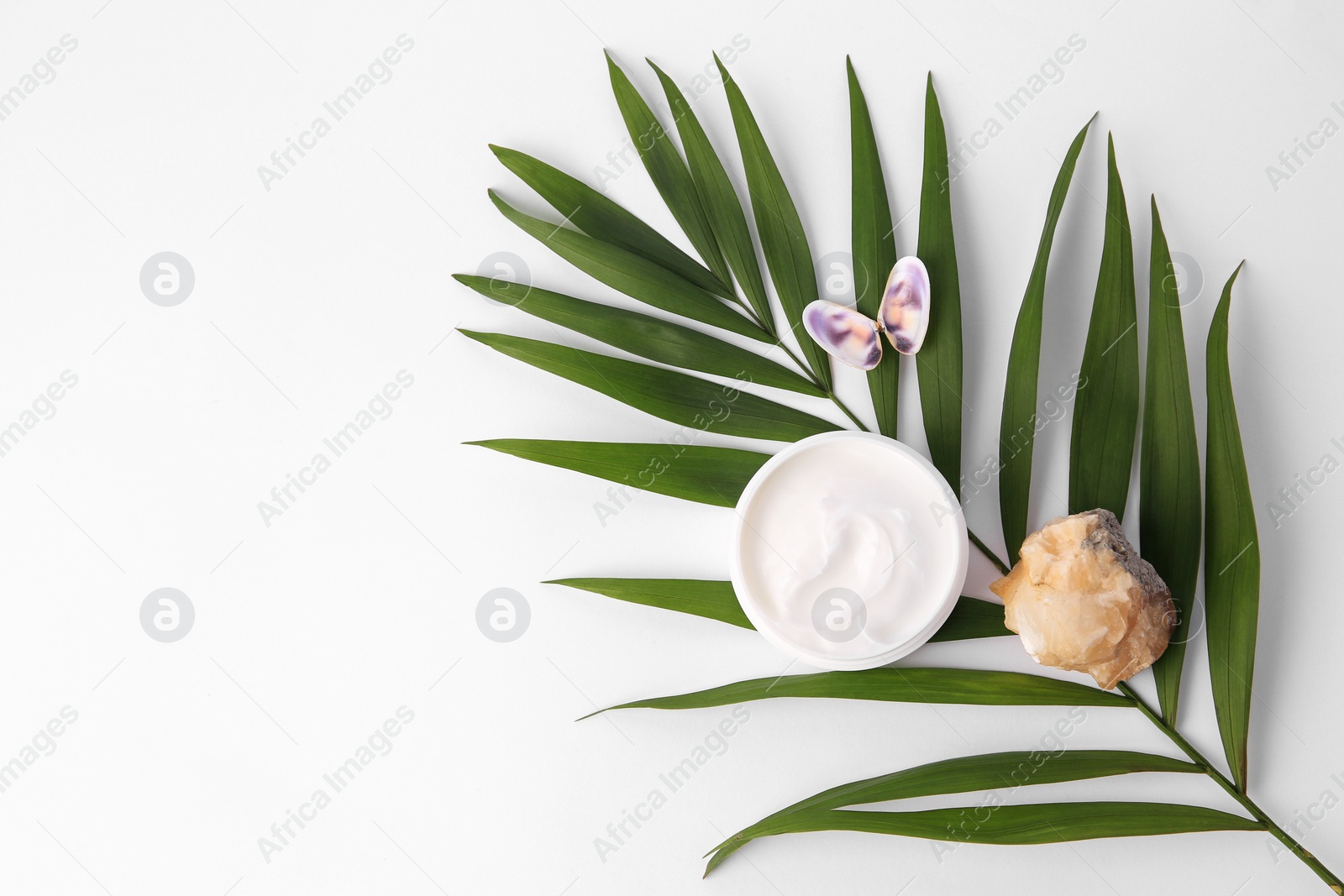 Photo of Jar of cream, shells, quartz gemstone and palm leaf on white background, flat lay. Space for text