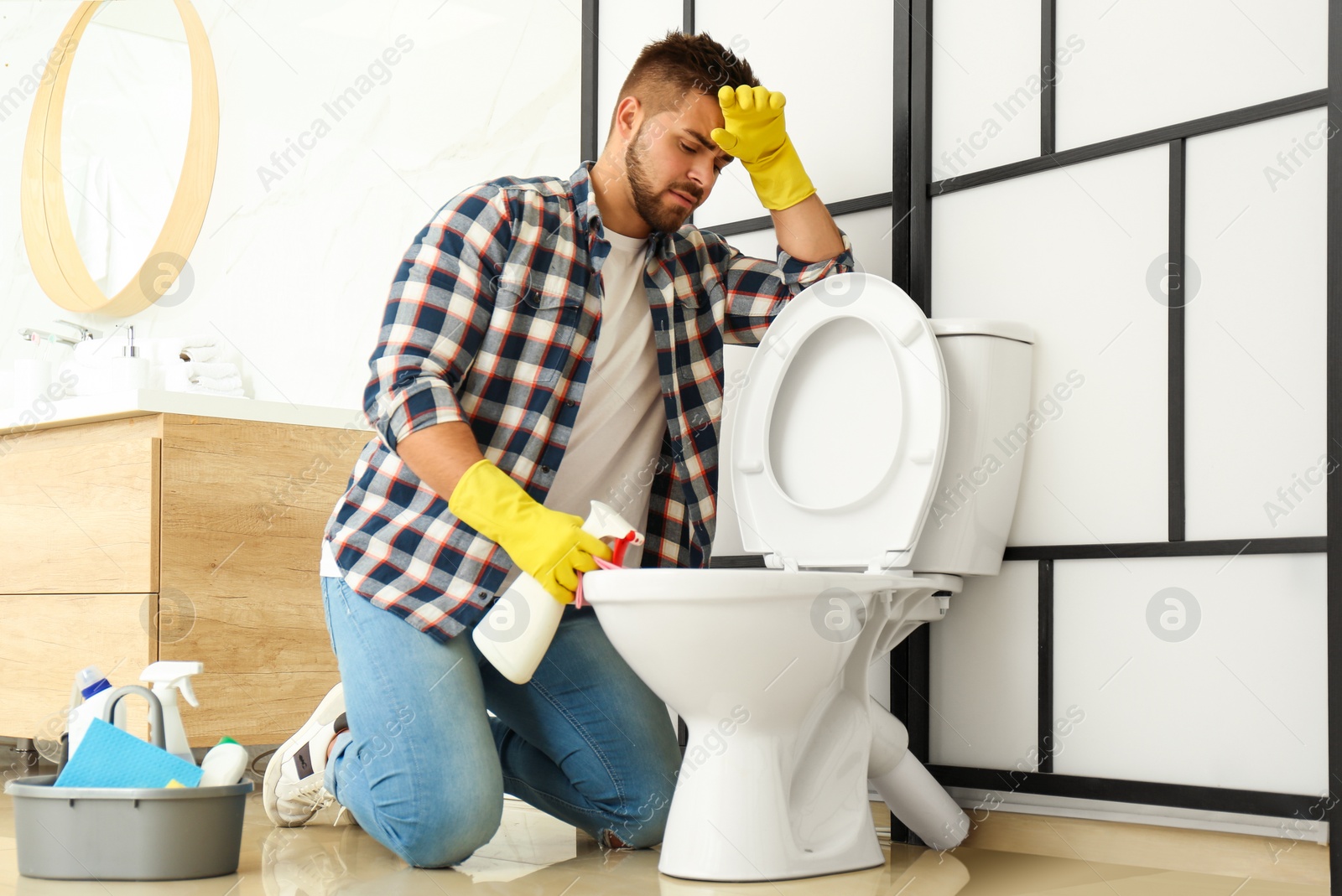 Photo of Young man feeling disgust while cleaning toilet bowl in bathroom