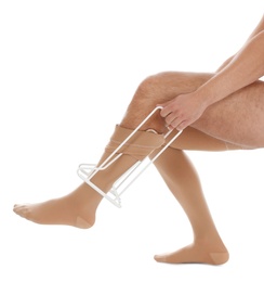 Man putting on compression garment with stocking donner against white background, closeup