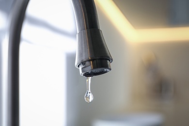 Photo of Water drop falling down from tap on blurred background, closeup