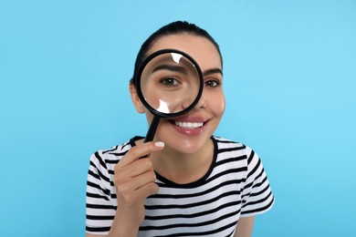 Woman looking through magnifier glass on light blue background