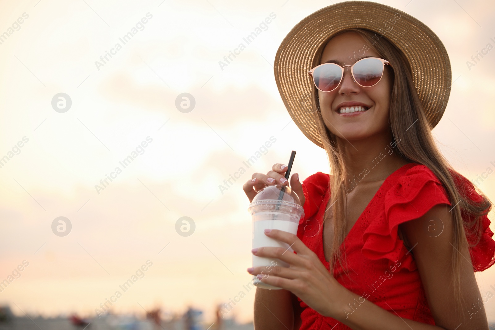 Photo of Beautiful young woman with tasty milk shake outdoors, space for text