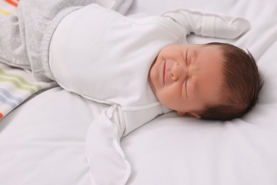 Cute newborn baby crying on white bed