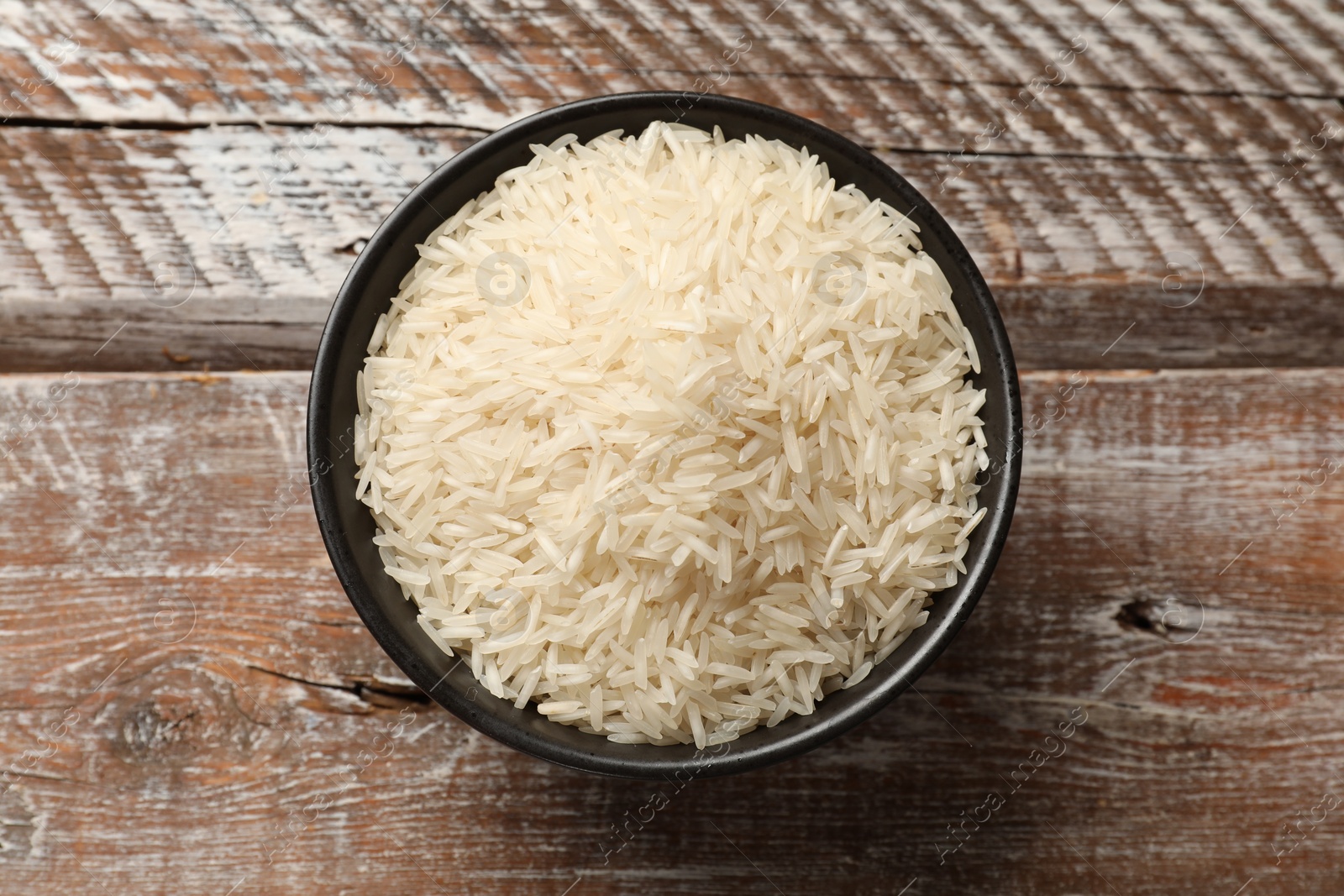 Photo of Raw basmati rice in bowl on wooden table, top view