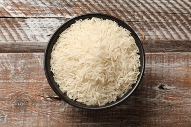 Photo of Raw basmati rice in bowl on wooden table, top view