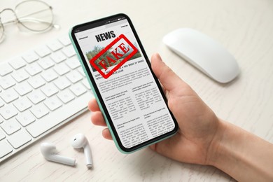 Image of Fake information. Woman using mobile phone to read news at wooden table, closeup