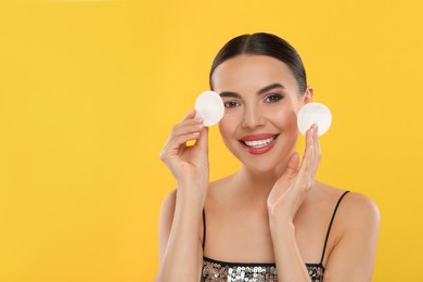 Photo of Beautiful woman holding cotton pads on orange background, space for text. Removing makeup