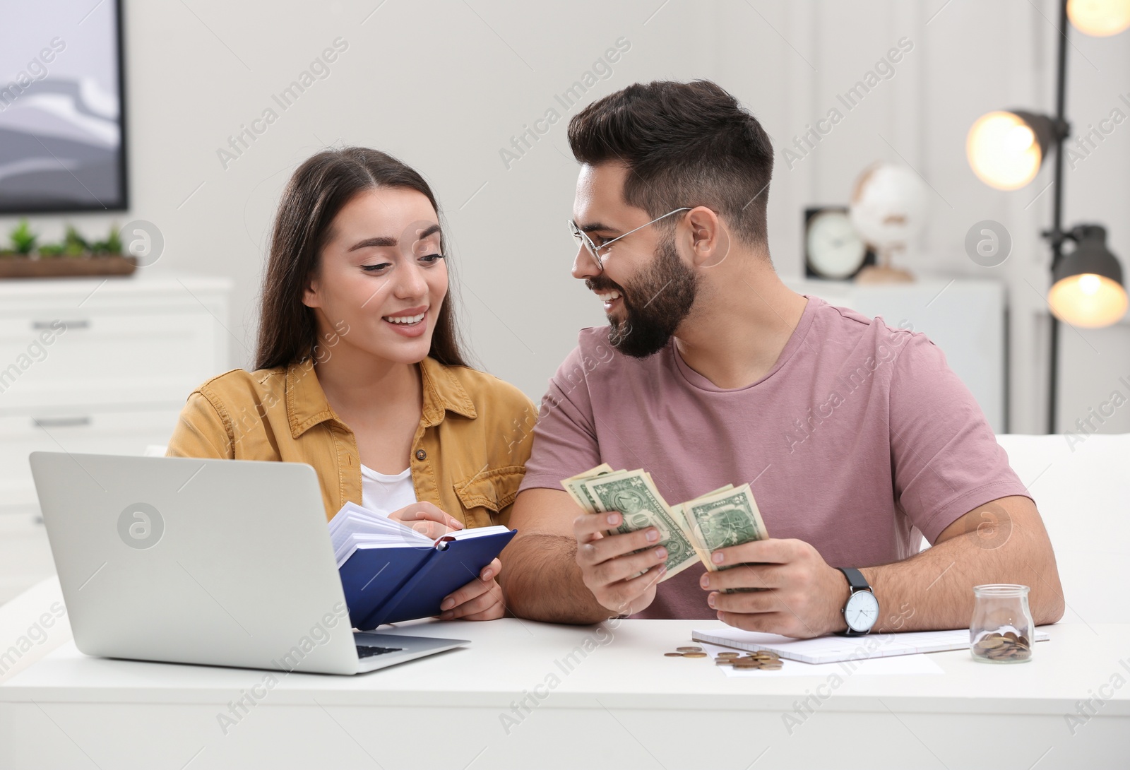 Photo of Happy young couple counting money at white table indoors