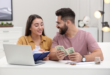 Happy young couple counting money at white table indoors