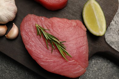 Raw tuna fillet with rosemary and lime wedge on grey table, top view