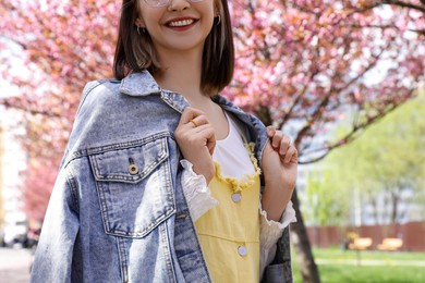 Photo of Beautiful young woman in park with blossoming sakura trees, closeup