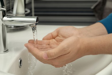 Photo of Man using water tap to wash hands in bathroom, closeup
