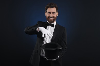 Photo of Happy magician showing magic trick with top hat on dark blue background