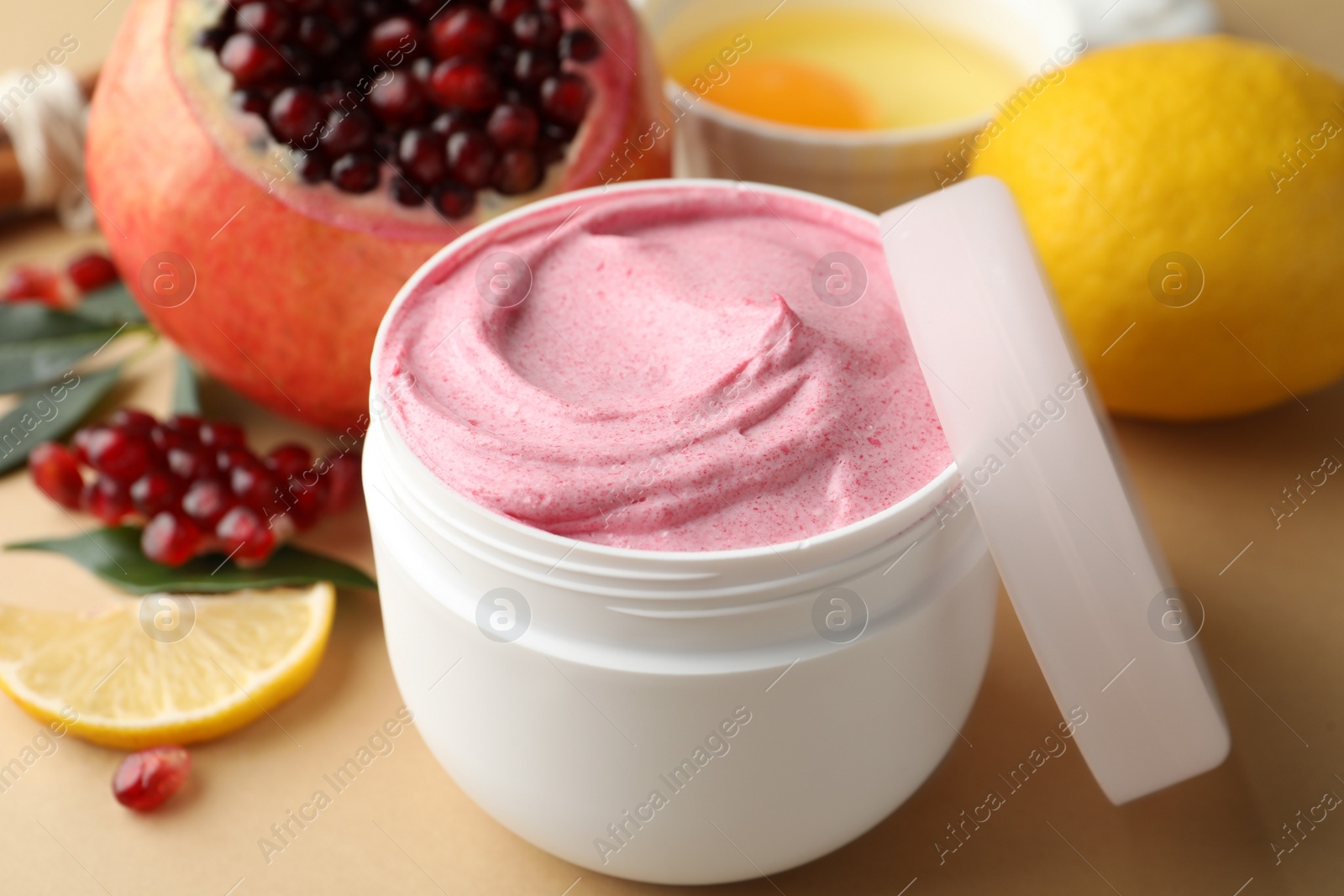 Photo of Jar of facial mask and fresh pomegranate on beige background, closeup. Natural organic cosmetics