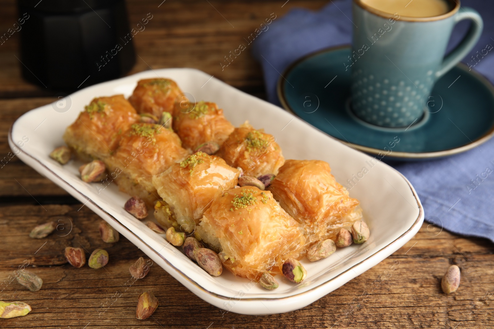 Photo of Delicious baklava with pistachios, hot drink and scattered nuts on wooden table, closeup