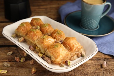 Delicious baklava with pistachios, hot drink and scattered nuts on wooden table, closeup