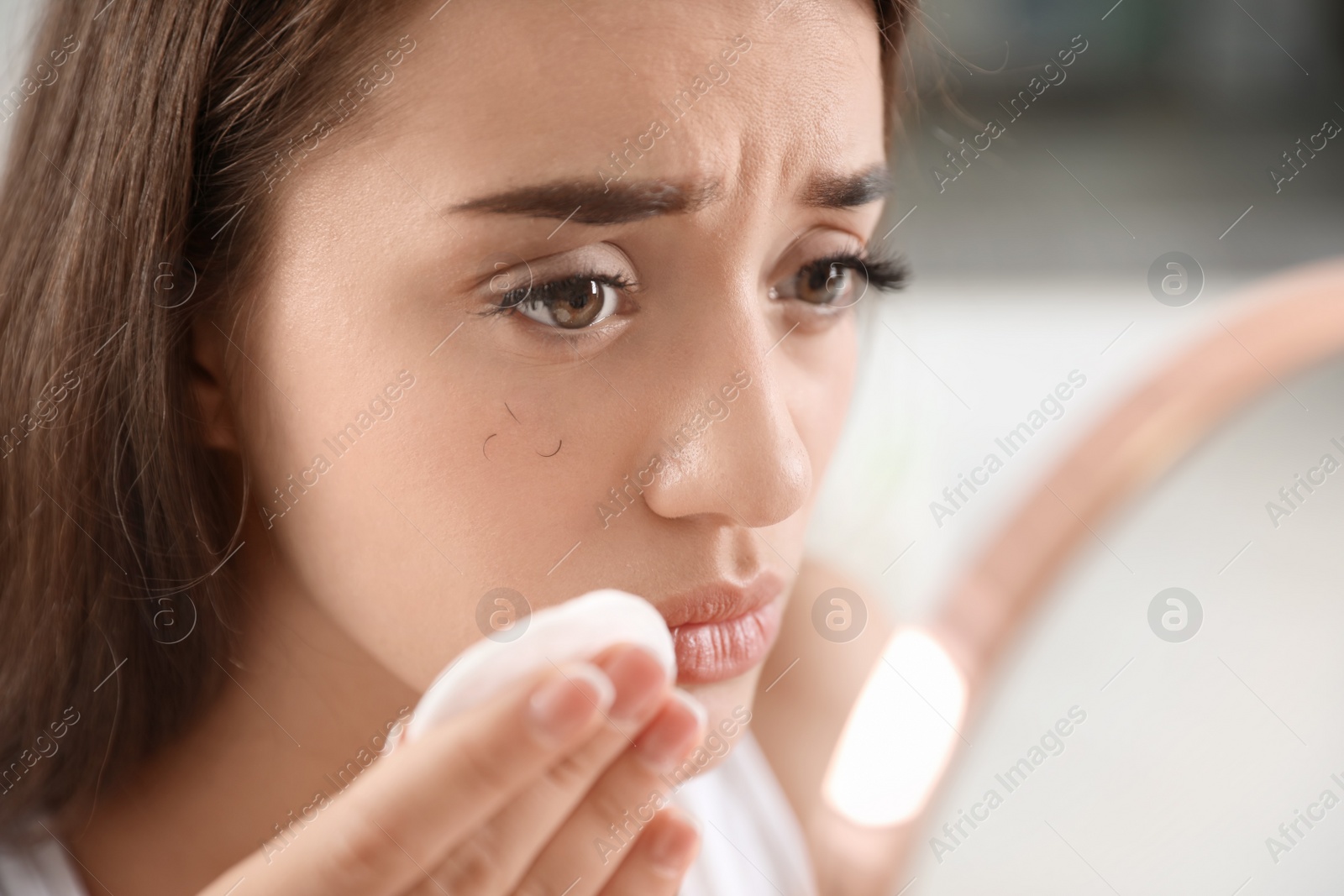 Photo of Young woman with eyelash loss problem removing makeup indoors