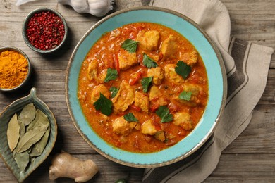 Photo of Delicious chicken curry and ingredients on wooden table, flat lay
