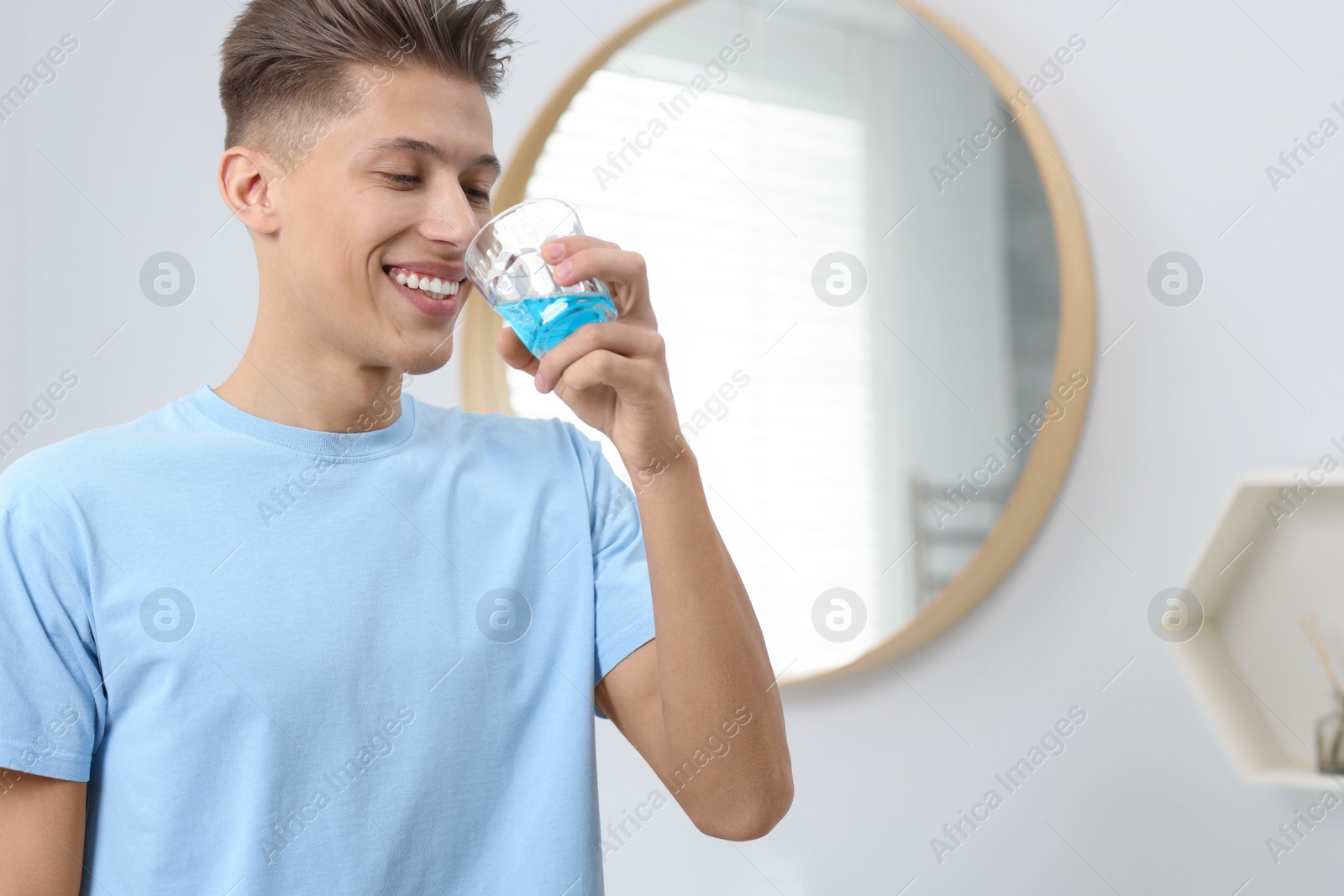 Photo of Young man using mouthwash in bathroom. Oral hygiene