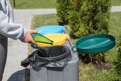 Photo of Woman throwing glass bottle in bin outdoors, closeup. Recycling concept