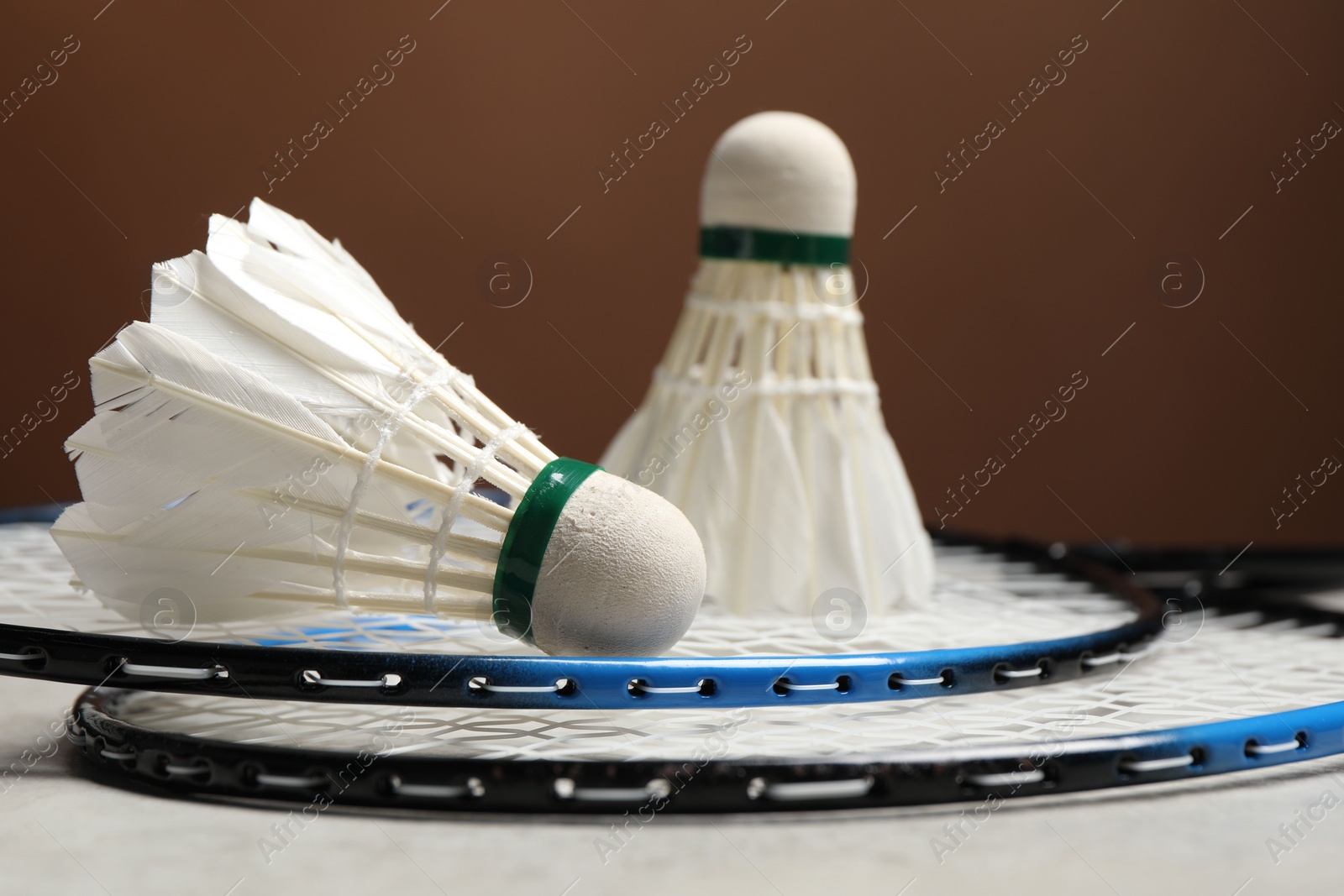 Photo of Feather badminton shuttlecocks and rackets on gray table against brown background, closeup