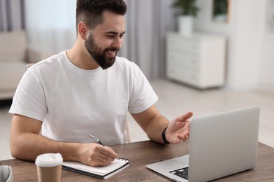 Young man using video chat during webinar at table in room