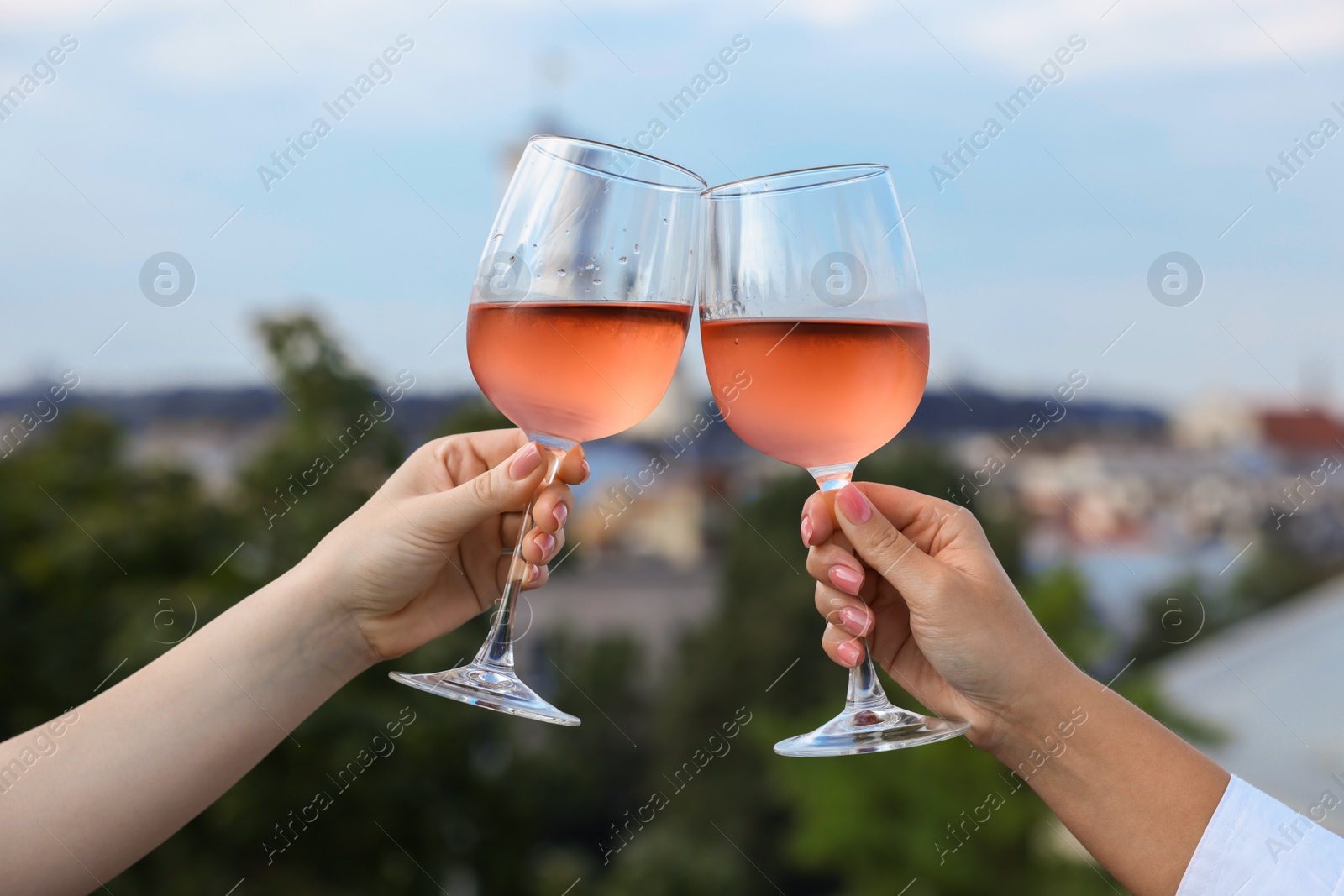 Photo of Women clinking glasses with rose wine outdoors, closeup