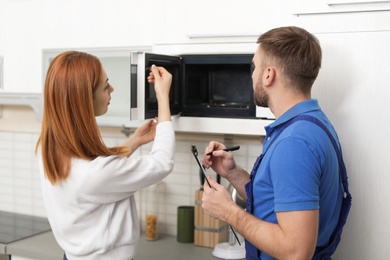 Housewife and repairman near microwave oven in kitchen