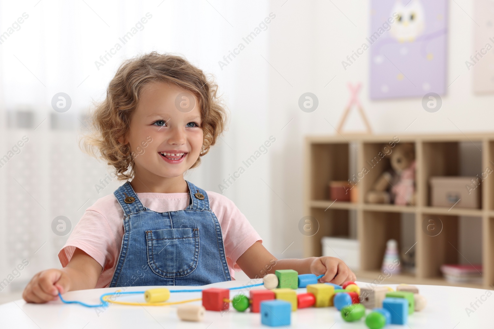 Photo of Motor skills development. Little girl playing with wooden pieces and string for threading activity at table indoors