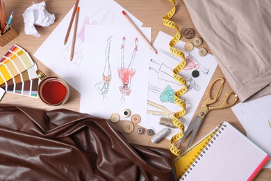 Photo of Sketches of clothes and different stuff on wooden table, flat lay. Fashion designer's workplace