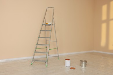 Photo of Metal stepladder near pale orange wall indoors. Room renovation