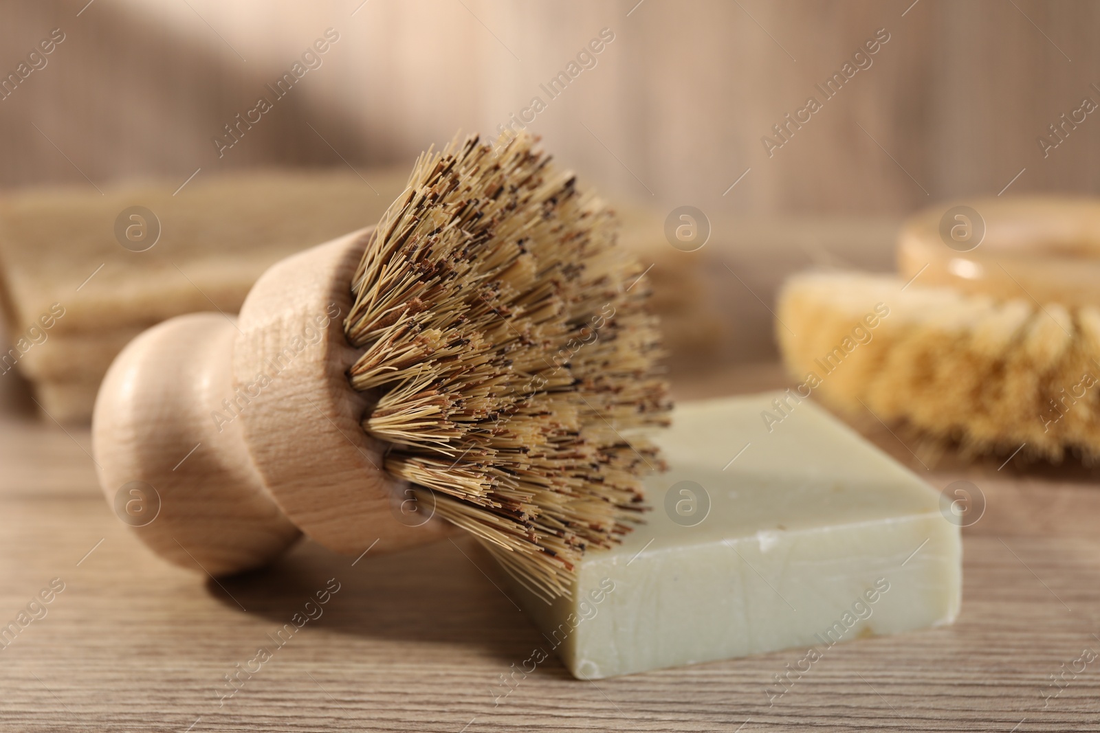 Photo of Cleaning brush and soap bar on wooden table, closeup