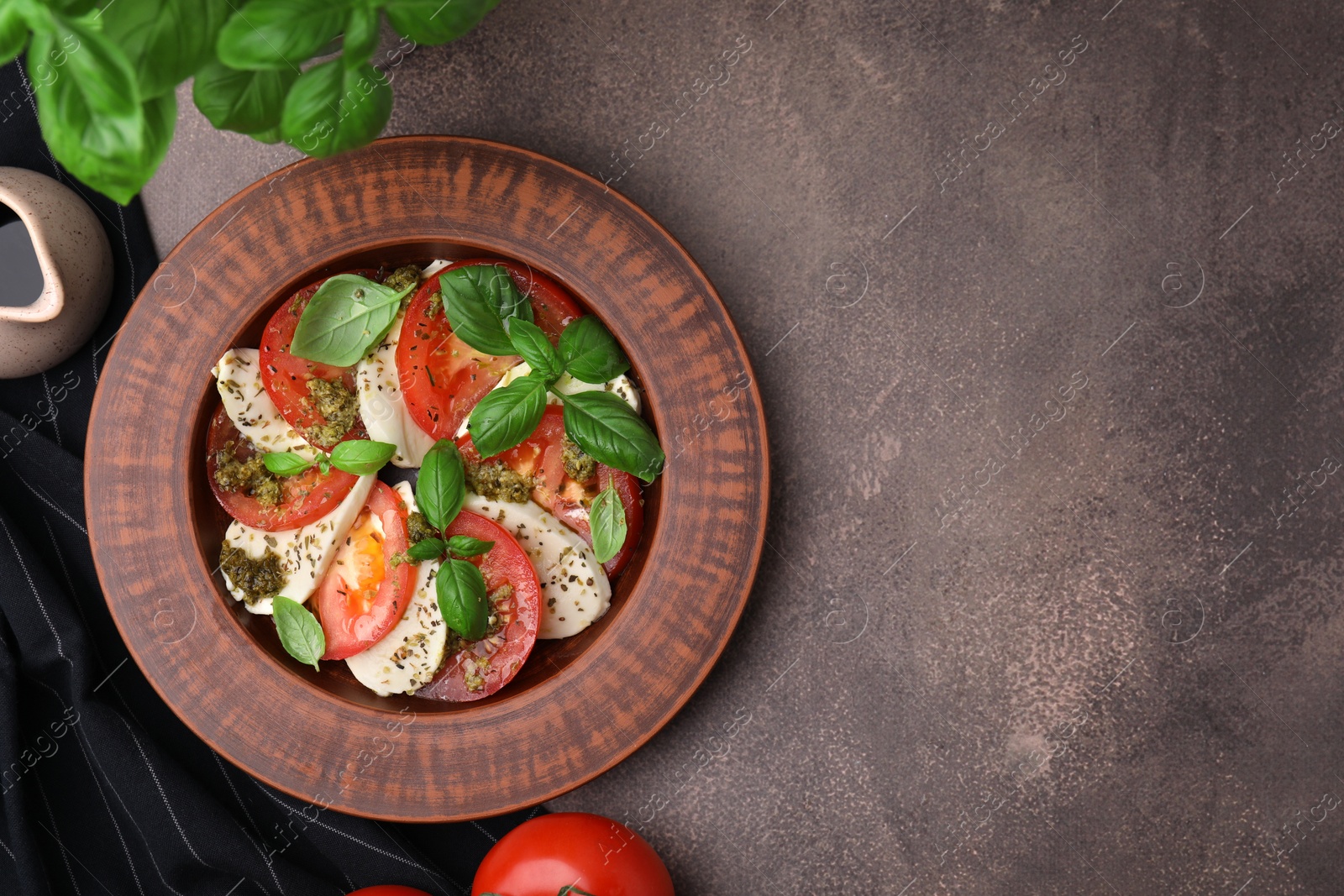 Photo of Plate of delicious Caprese salad with pesto sauce and ingredients on brown textured table, flat lay. Space for text