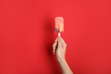 Photo of Woman holding berry popsicle on red background, closeup