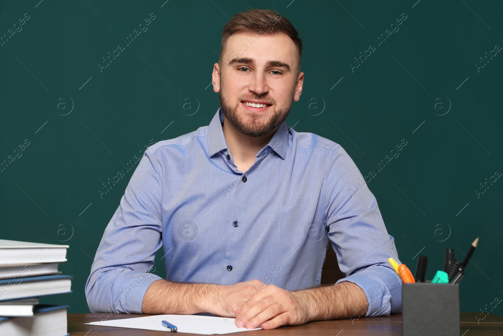 Photo of Portrait of young teacher at table against green background