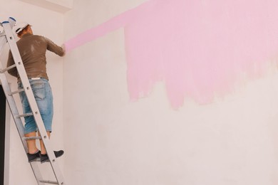 Photo of Decorator painting wall with brush indoors. Space for text