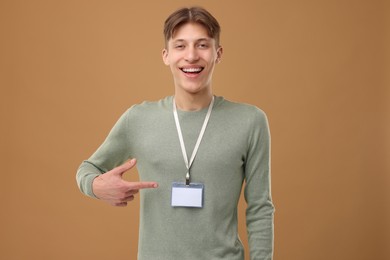 Happy man pointing at blank badge on light brown background